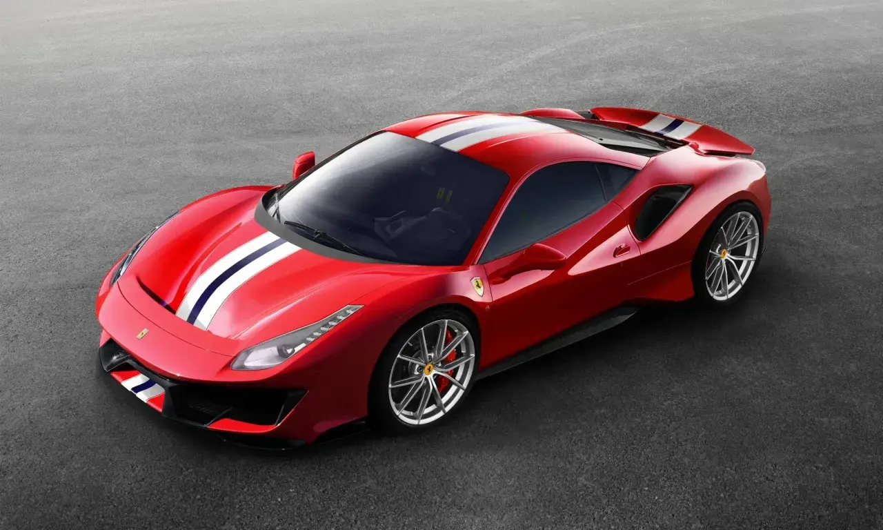 Czerwone Ferrari Pista z białymi i niebieskimi pasami na masce i dachu, zaparkowane na szarym asfalcie.