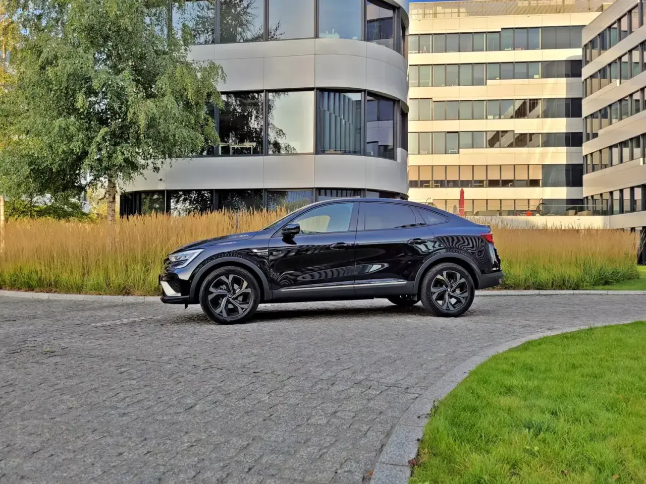 Elegancki, czarny Renault Arkana na tle nowoczesnych budynków biurowych.