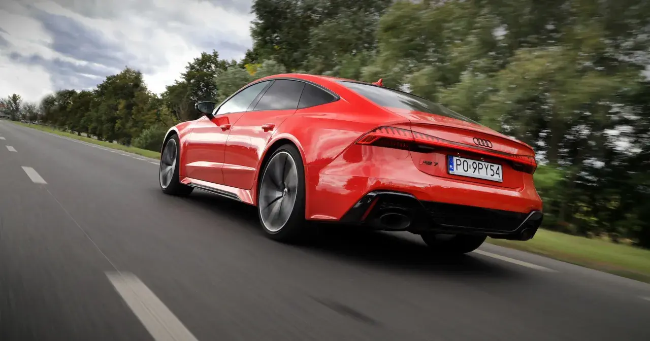 Czerwone Audi RS 7 pędzi po drodze, otoczone zielenią drzew.