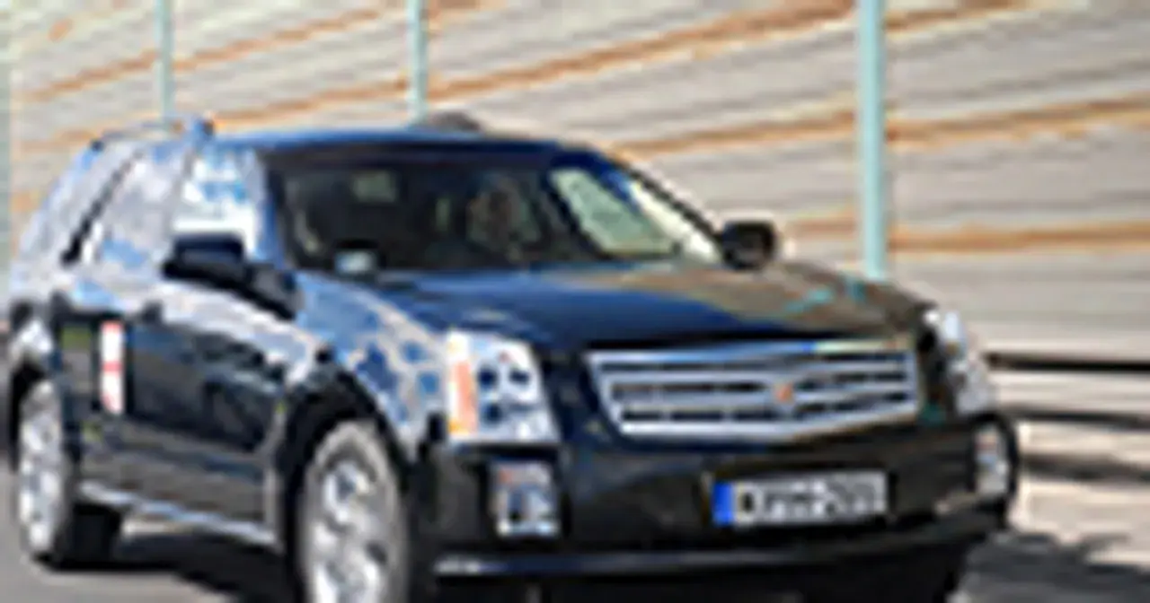 Czarny Cadillac SRX z przyciemnianymi szybami i chromowanymi detalami jedzie po drodze.