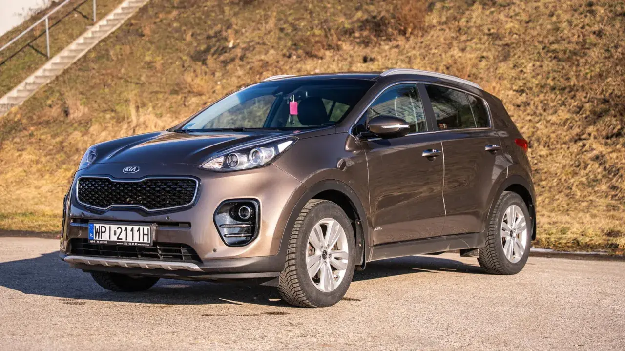 Brązowy Kia Sportage 2020 zaparkowany na tle suchej trawy i schodów.