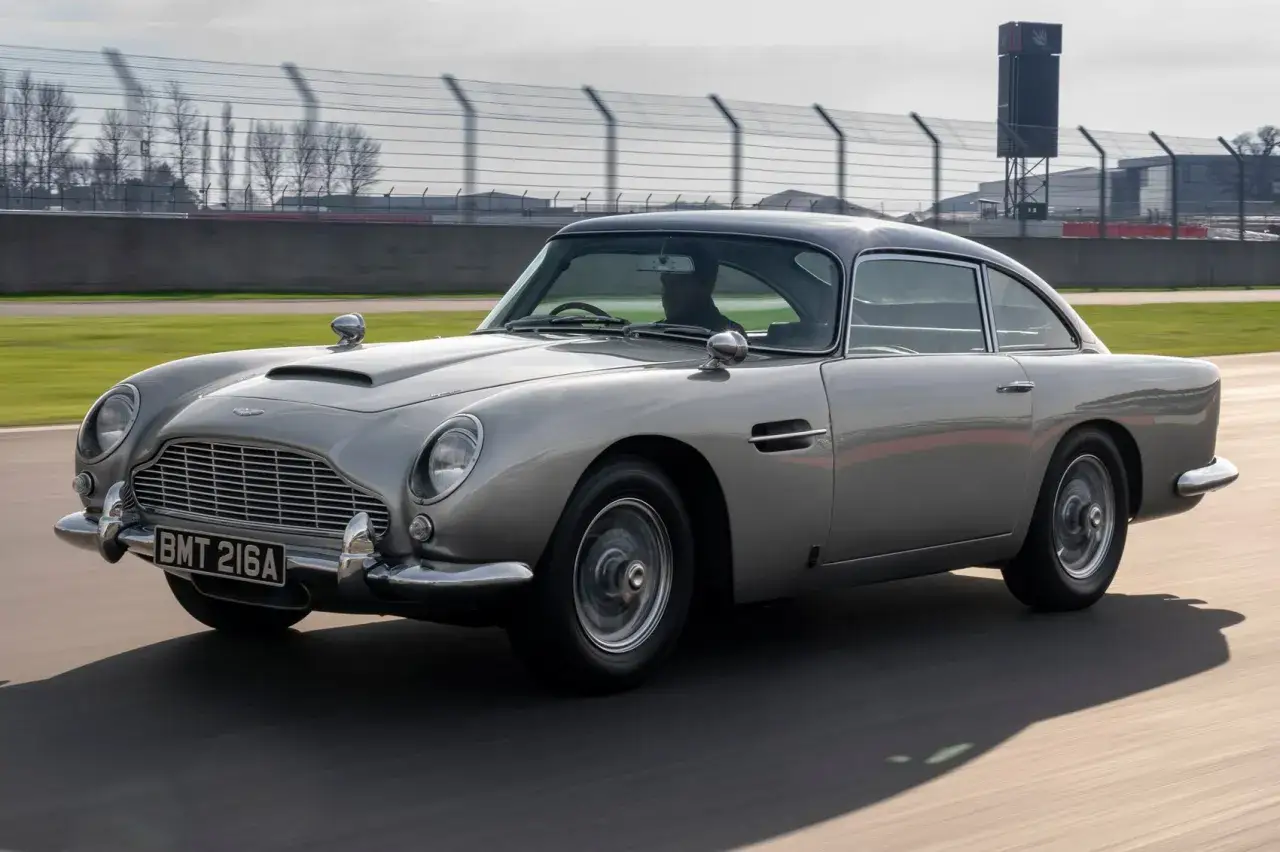 Srebrny Aston Martin DB5 pędzi po torze wyścigowym, jego klasyczna sylwetka budzi wspomnienia o przygodach Jamesa Bonda.