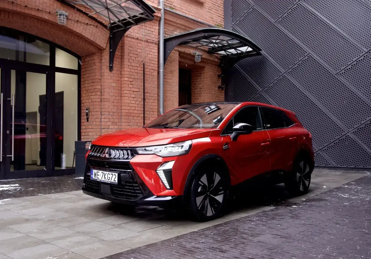 Czerwony SUV, jeden z nowych mitsubishi modele, zaparkowany przed budynkiem z cegły i metalową fasadą.