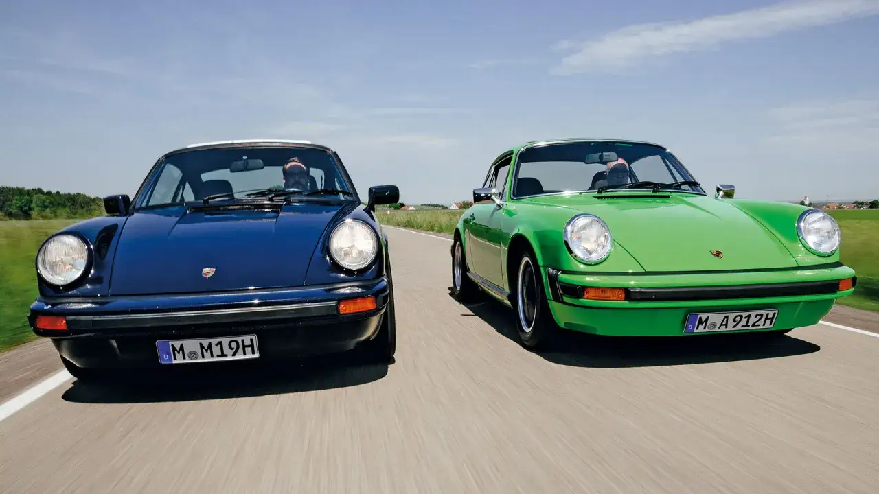 Dwa klasyczne Porsche 912, granatowe i zielone, jadą obok siebie po wiejskiej drodze.