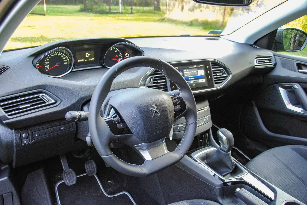 Wnętrze Peugeota 308 z 2015 roku: kierownica, deska rozdzielcza z ekranem dotykowym i zegarami.