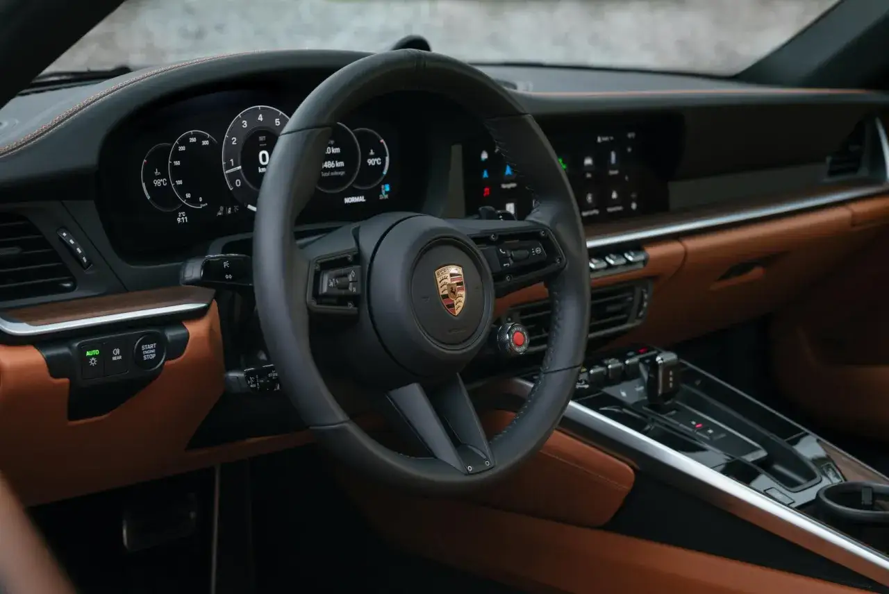 Wnętrze Porsche 992 z brązową skórą i cyfrowymi zegarami. Kierownica z logo Porsche.