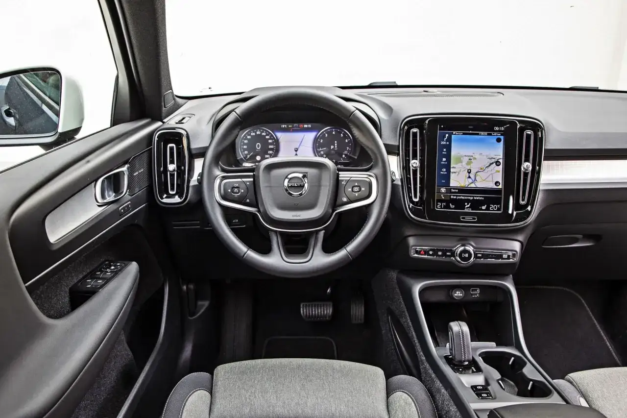 Wnętrze Volvo XC40, z ekranem nawigacji i cyfrowymi zegarami. Kierownica i konsola środkowa. Wiele osób szuka volvo xc40 opinie.