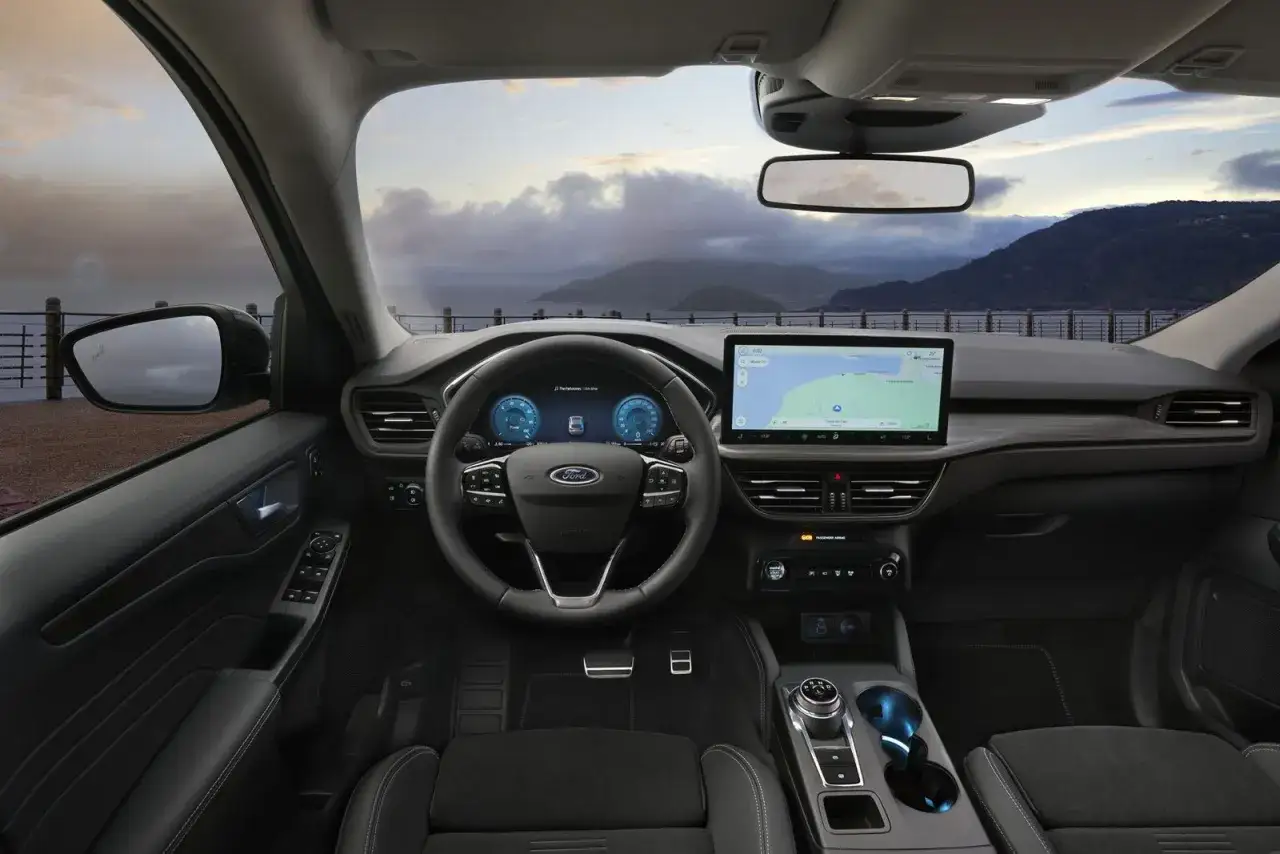 Wnętrze nowego Ford Kuga z nowoczesnym ekranem nawigacji i cyfrowymi zegarami. Widok na morze i góry przez przednią szybę.