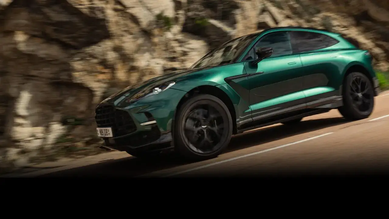 Zielony Aston Martin DBX 707 pędzi po krętej drodze, otoczony skalistym krajobrazem.