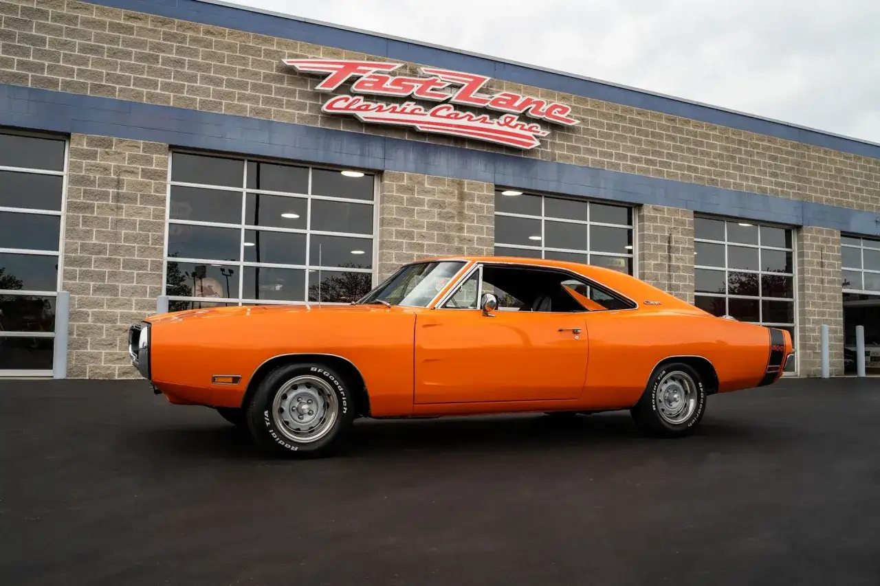 Pomarańczowy Dodge Charger 1970 z czarnym pasem z tyłu, zaparkowany przed budynkiem Fast Lane Classic Cars Inc.