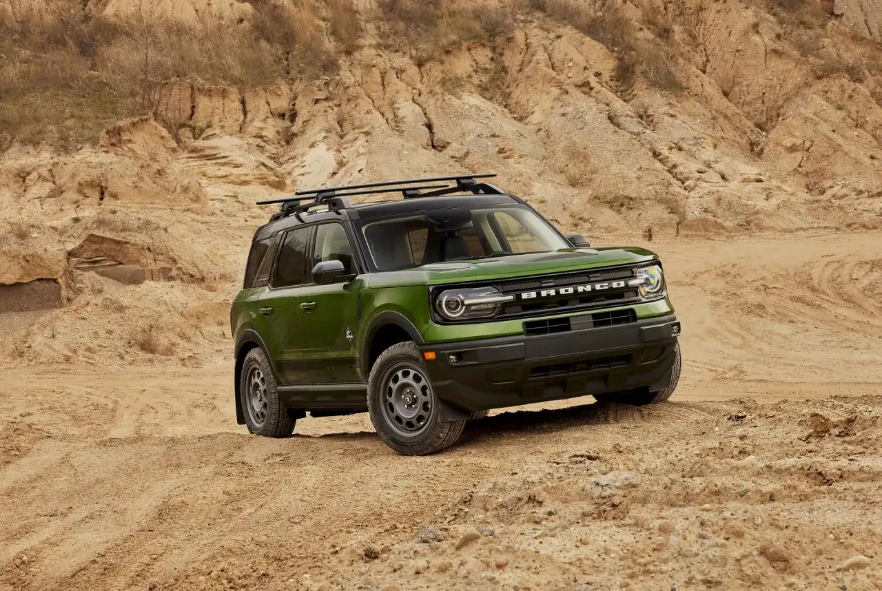Zielony Ford Bronco Sport z bagażnikiem dachowym na piaszczystym, pustynnym terenie.