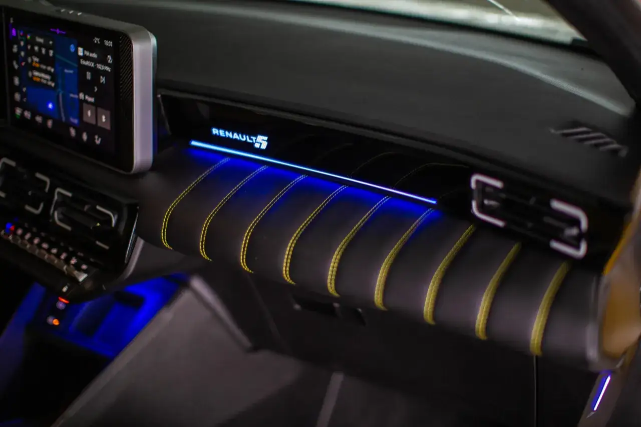 Wnętrze nowego Renault 5 z niebieskim podświetleniem i żółtymi szwami.