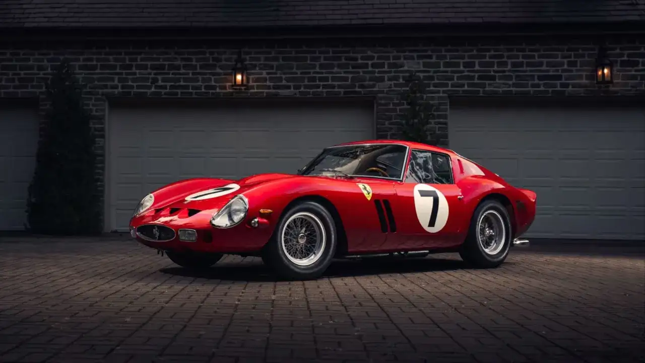 Czerwone Ferrari 250 GTO z numerem 7 na białym tle, zaparkowane na podjeździe przed garażem.