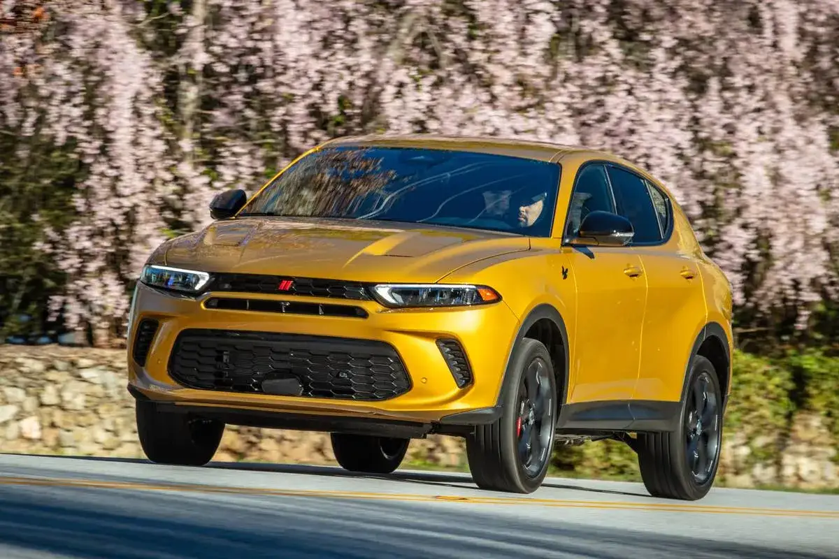 Żółty Dodge Hornet pędzi po drodze wśród kwitnących drzew. Nowe modele Dodge'a zachwycają.