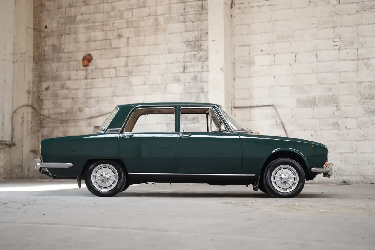 Klasyczny, ciemnozielony fiat 130 z lat 70. stoi w opuszczonym magazynie, jego elegancka linia podkreślona przez surowe, ceglane ściany.