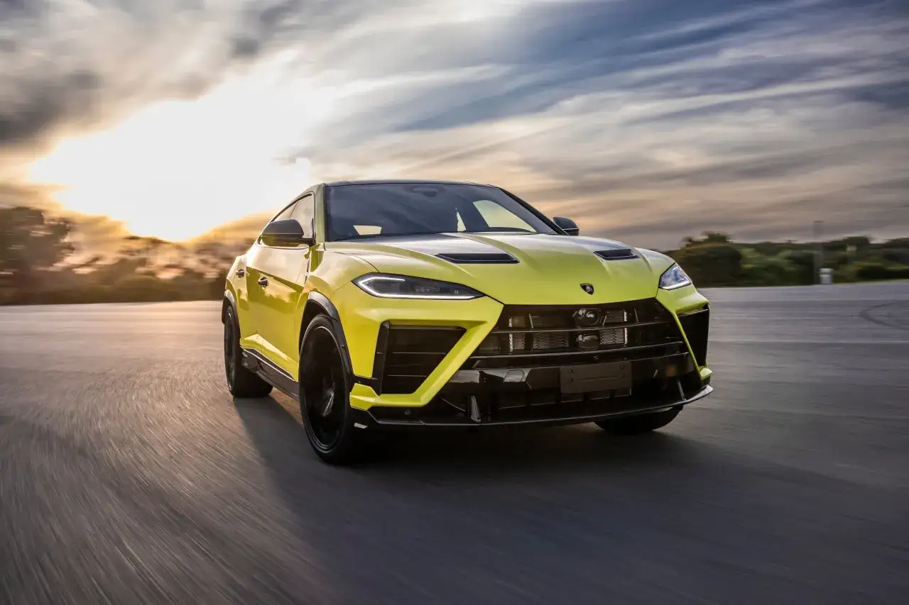 Żółty Lambo Urus pędzi po drodze podczas zachodu słońca, chmury tworzą dramatyczne tło.