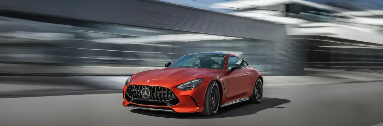 Pomarańczowy Mercedes-AMG GT 63 S pędzi ulicą, zostawiając za sobą rozmyte tło nowoczesnej architektury.
