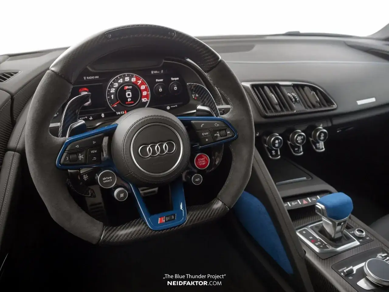 Wnętrze sportowego Audi R8 z niebieskimi akcentami i cyfrowym kokpitem. Kierownica obszyta alcantarą i włóknem węglowym.