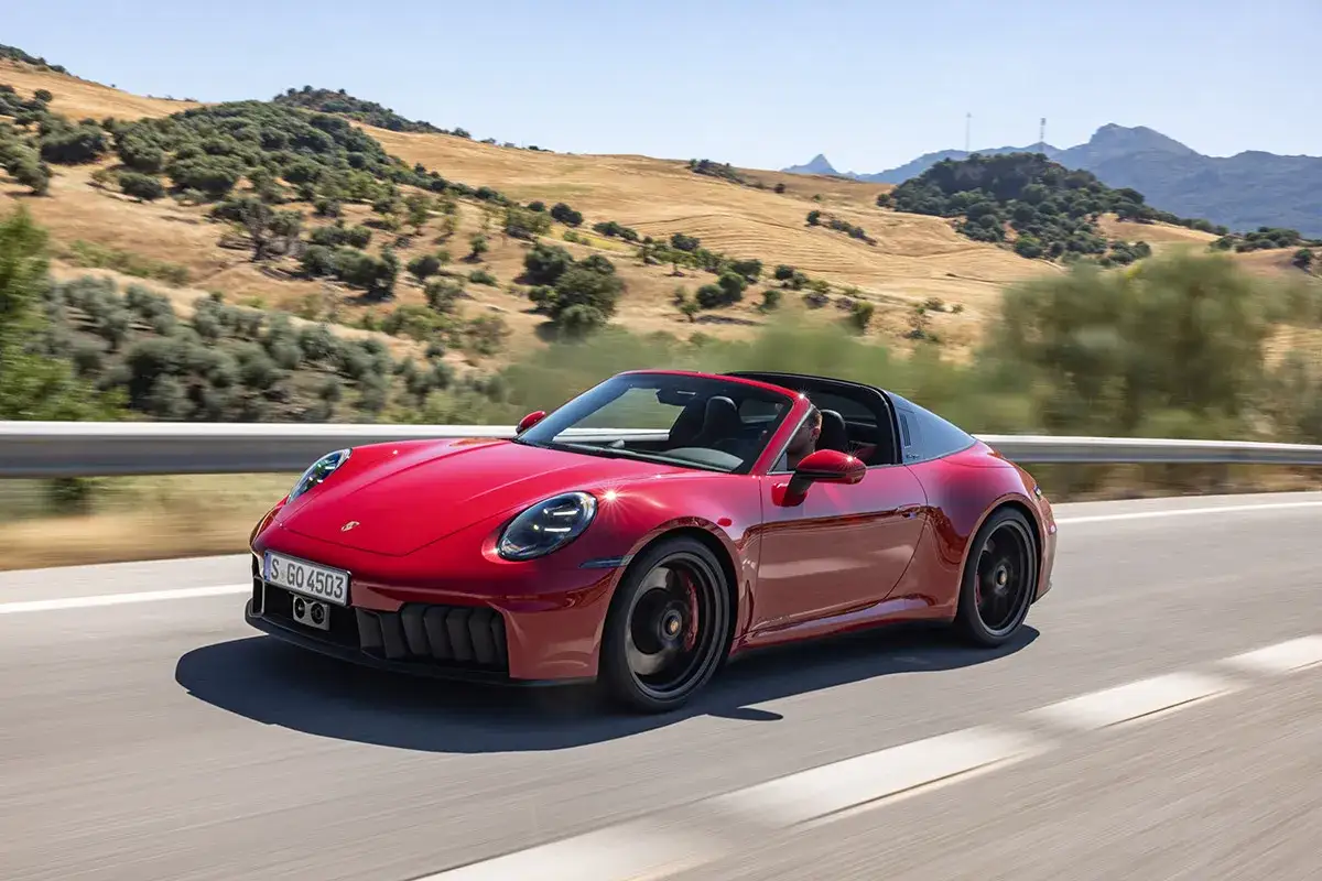 Czerwony Porsche 911 GTS Targa z otwartym dachem sunie po krętej drodze wśród wzgórz.