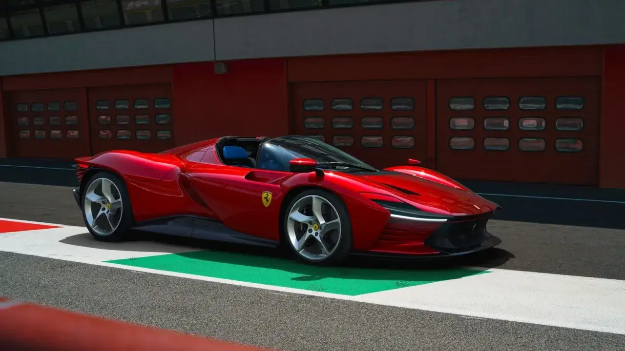 Czerwone Ferrari SP3 na torze wyścigowym, z niebieskimi siedzeniami i charakterystycznymi felgami.