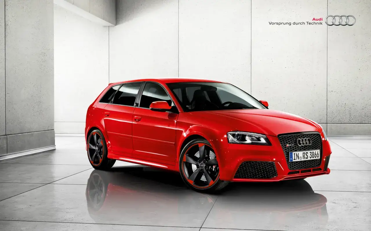 Czerwone Audi RS3 w nowoczesnym garażu, z czarnymi felgami i czerwonymi akcentami.