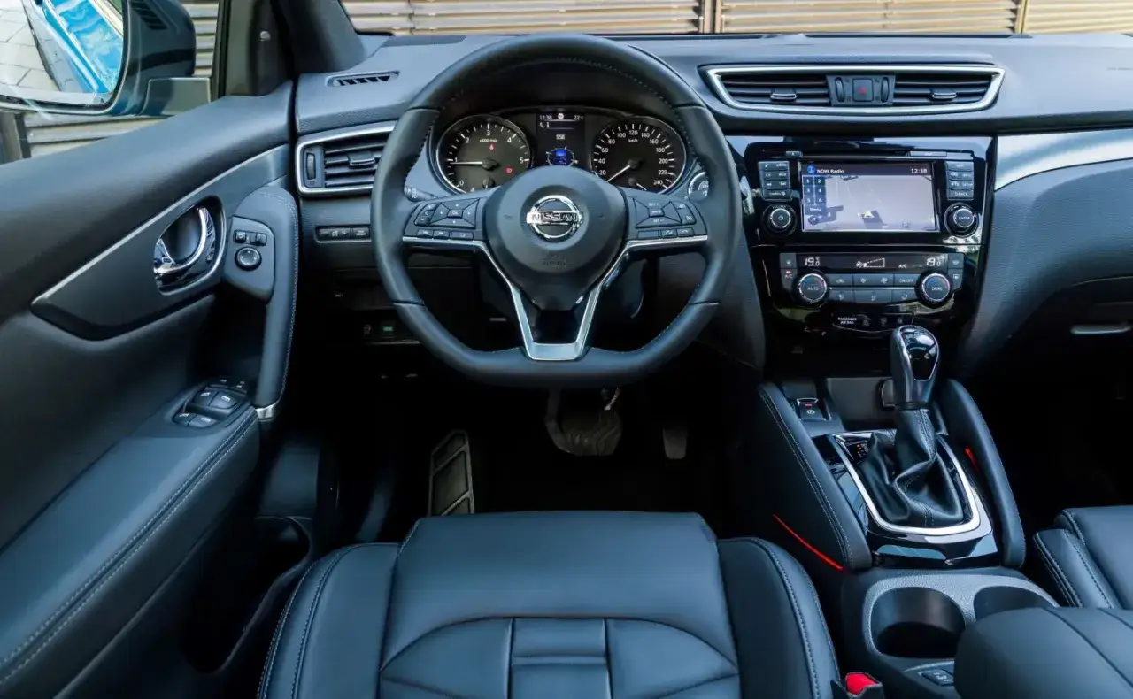 Wnętrze nissan qashqai 2018: czarna skórzana tapicerka, kierownica, deska rozdzielcza z ekranem nawigacji i panelem klimatyzacji.