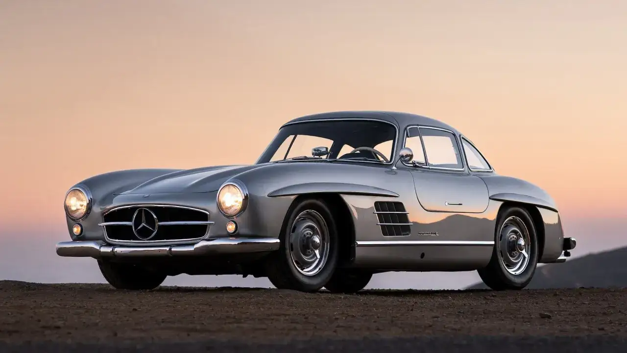 Srebrny Mercedes 300SL Gullwing, ikona motoryzacji, lśni na tle zachodzącego słońca.