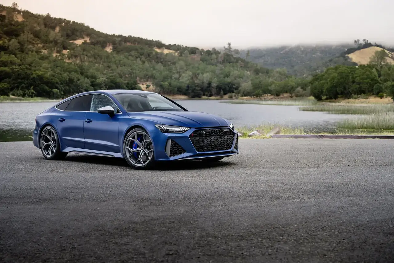 Niebieski Audi RS 7 prezentuje się majestatycznie nad jeziorem, gotowy na przygodę w malowniczym krajobrazie.