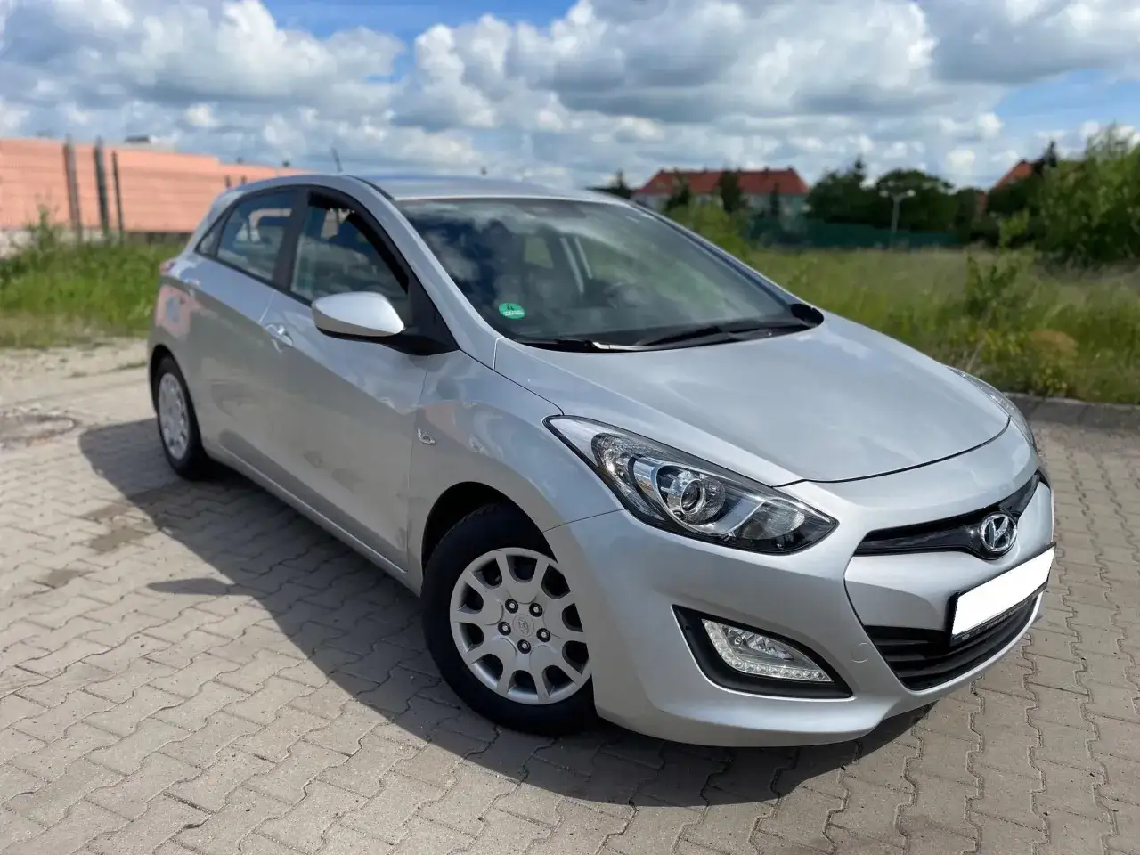 Srebrny Hyundai i30 1.4 benzyna, często chwalony w opiniach za niezawodność i ekonomiczność, zaparkowany na kostce brukowej.