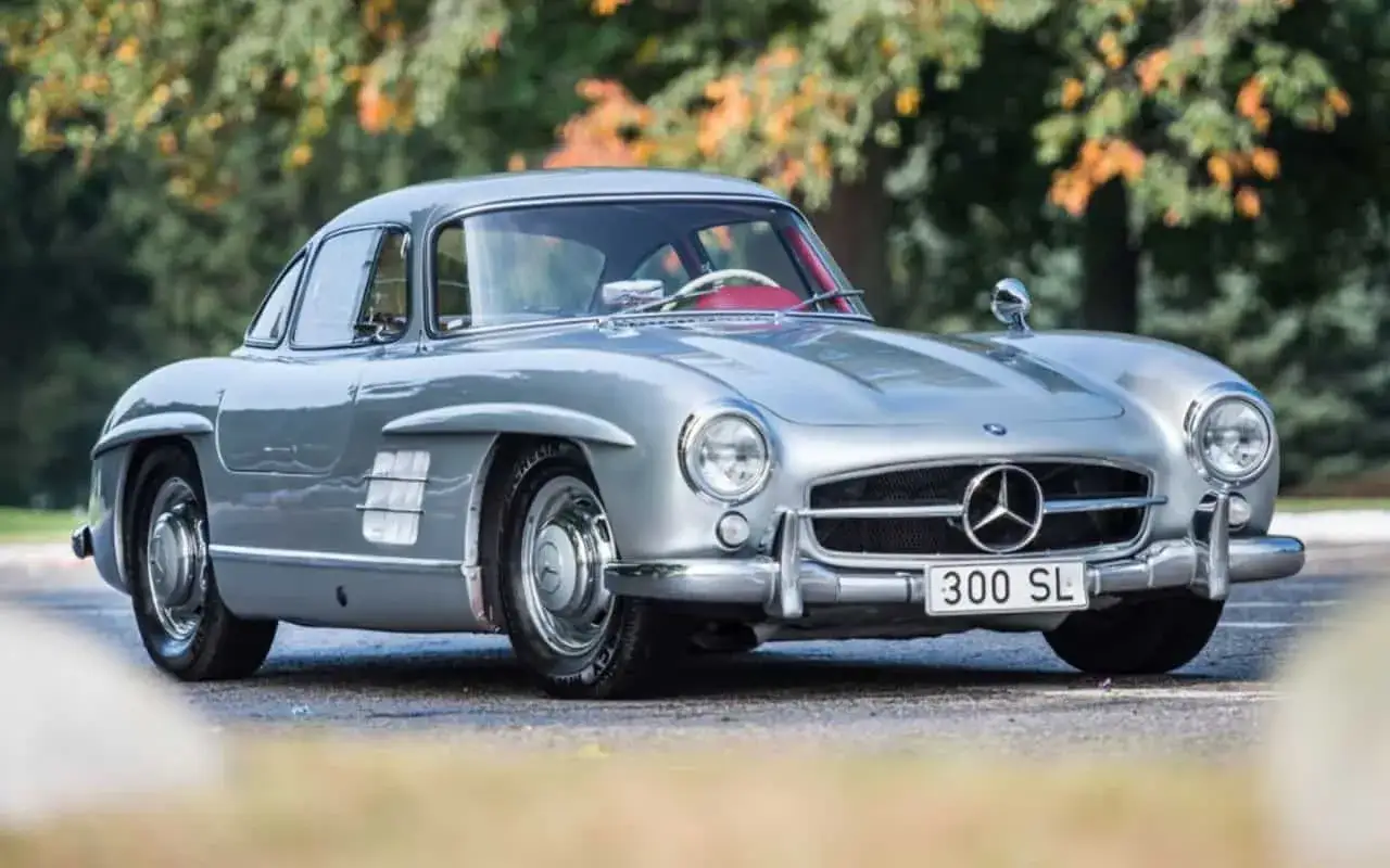 Srebrny Mercedes-Benz 300 SL, ikona motoryzacji, prezentuje swoje klasyczne linie na tle jesiennej zieleni.