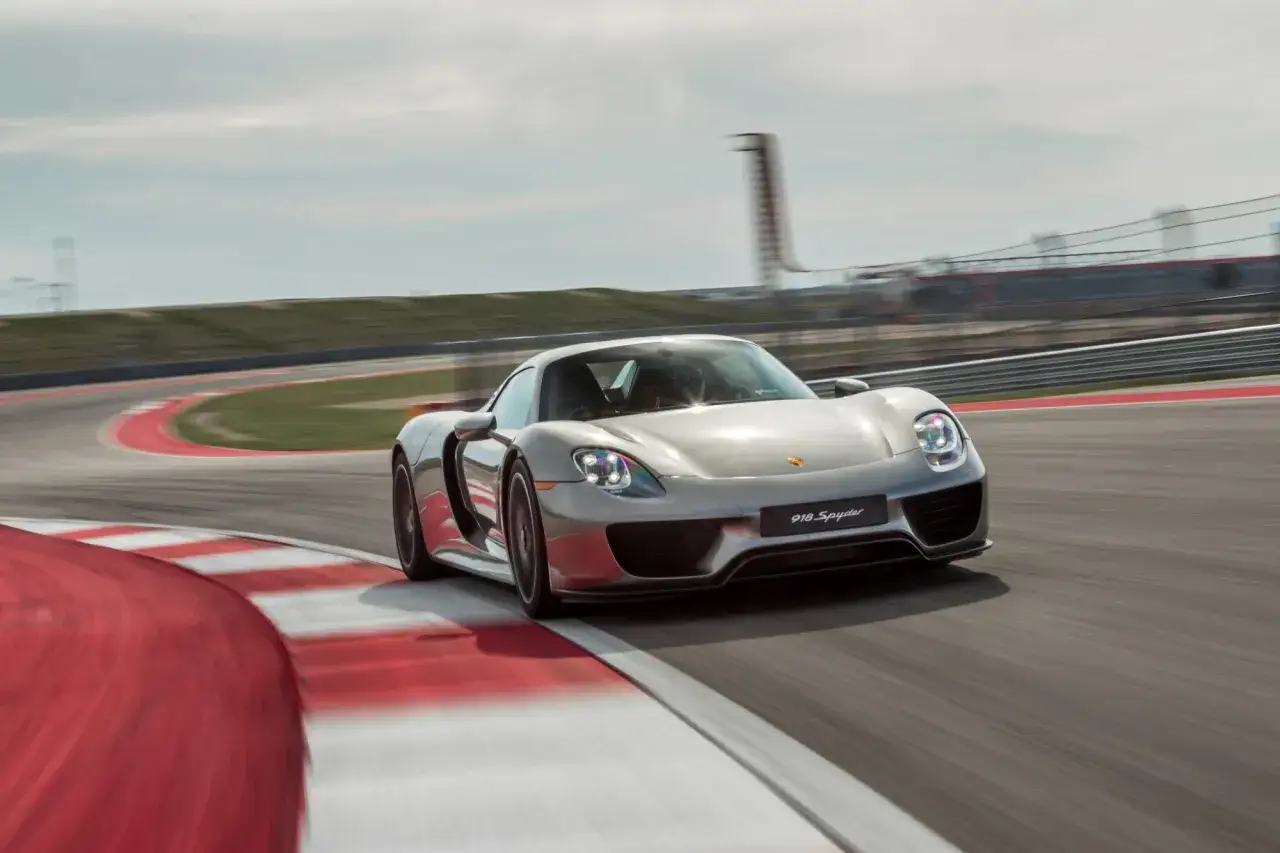 Srebrny Porsche 918 Spyder pędzi po torze wyścigowym, pokonując zakręt z rozmytymi czerwono-białymi krawężnikami.