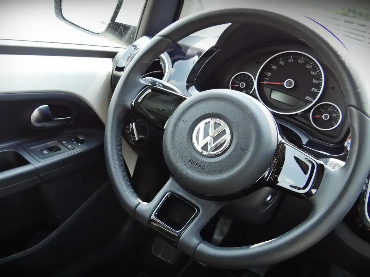 Wnętrze volkswagen up: kierownica z logo, deska rozdzielcza z prędkościomierzem i wskaźnikami, panel drzwi z przyciskami.