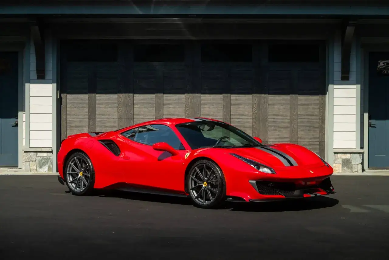 Czerwone Ferrari Pista z szarymi pasami na masce, zaparkowane przed garażem.