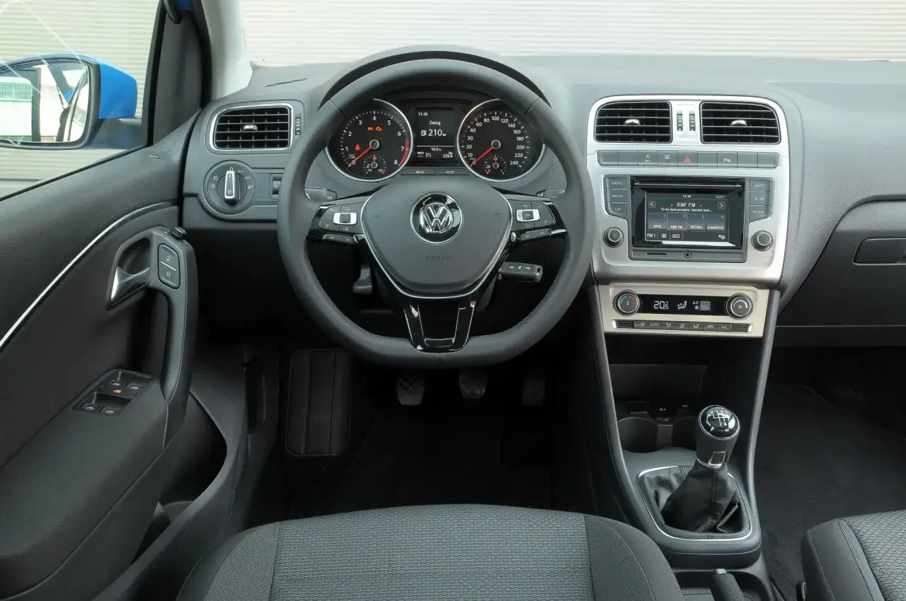 Wnętrze VW Polo 2010: kierownica z przyciskami, zegary, radio, nawiewy i dźwignia zmiany biegów.