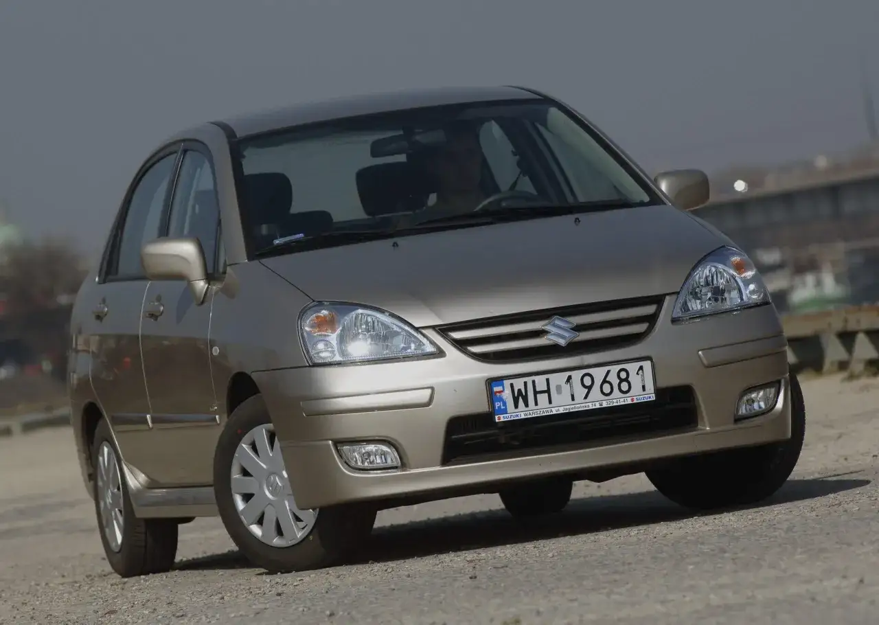 Złoty Suzuki Liana z tablicą rejestracyjną WH 19681 stoi na drodze.