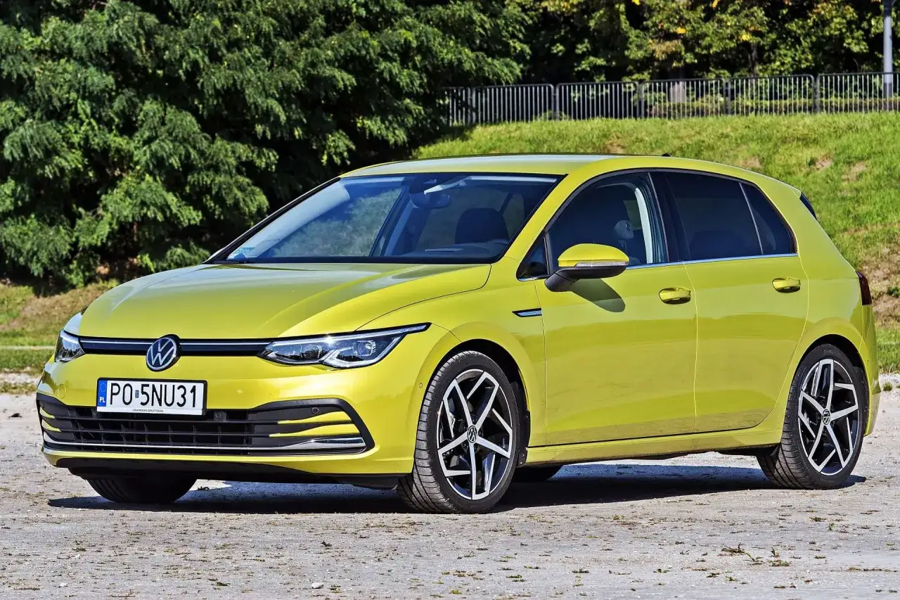 Żółty Volkswagen Golf 8, jeden z wielu popularnych volkswagen nazwy modeli, zaparkowany na tle zieleni.