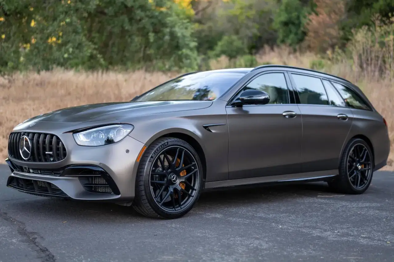 Matowy, grafitowy Mercedes E63 AMG kombi z pomarańczowymi zaciskami hamulcowymi i czarnymi felgami, zaparkowany na tle natury.