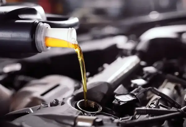 Wlewam olej do silnika Toyoty Yaris 1.0. Złoty płyn spływa z butelki do otworu.