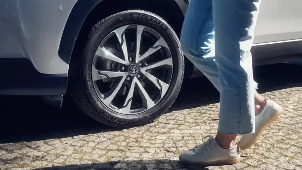 Osoba w jeansach i białych butach zbliża się do Toyoty Corolli. Dowiedz się, jak zresetować czujnik ciśnienia w oponach.