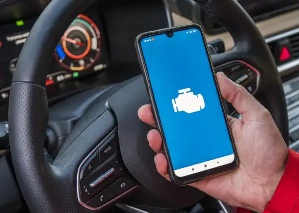 Ręka trzyma smartfon z ikoną silnika, gotowy do diagnostyki Toyoty. Jaki program do Toyoty z ELM327?